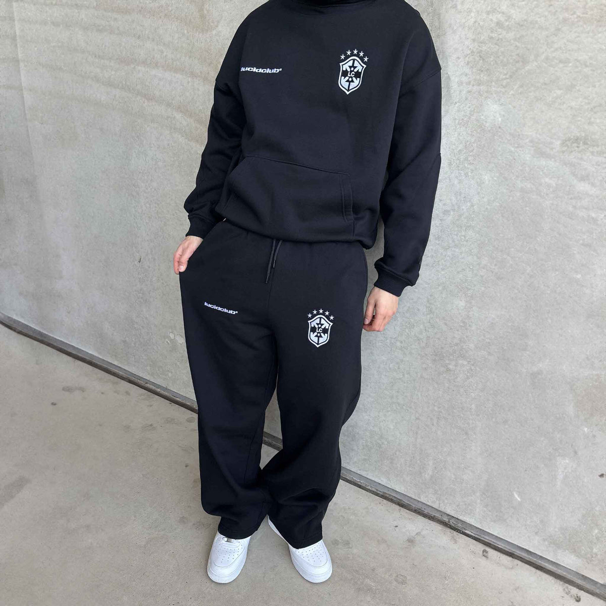 Brazil Hoodie und Brazil Sweatpants Black am Model vor Betonwand