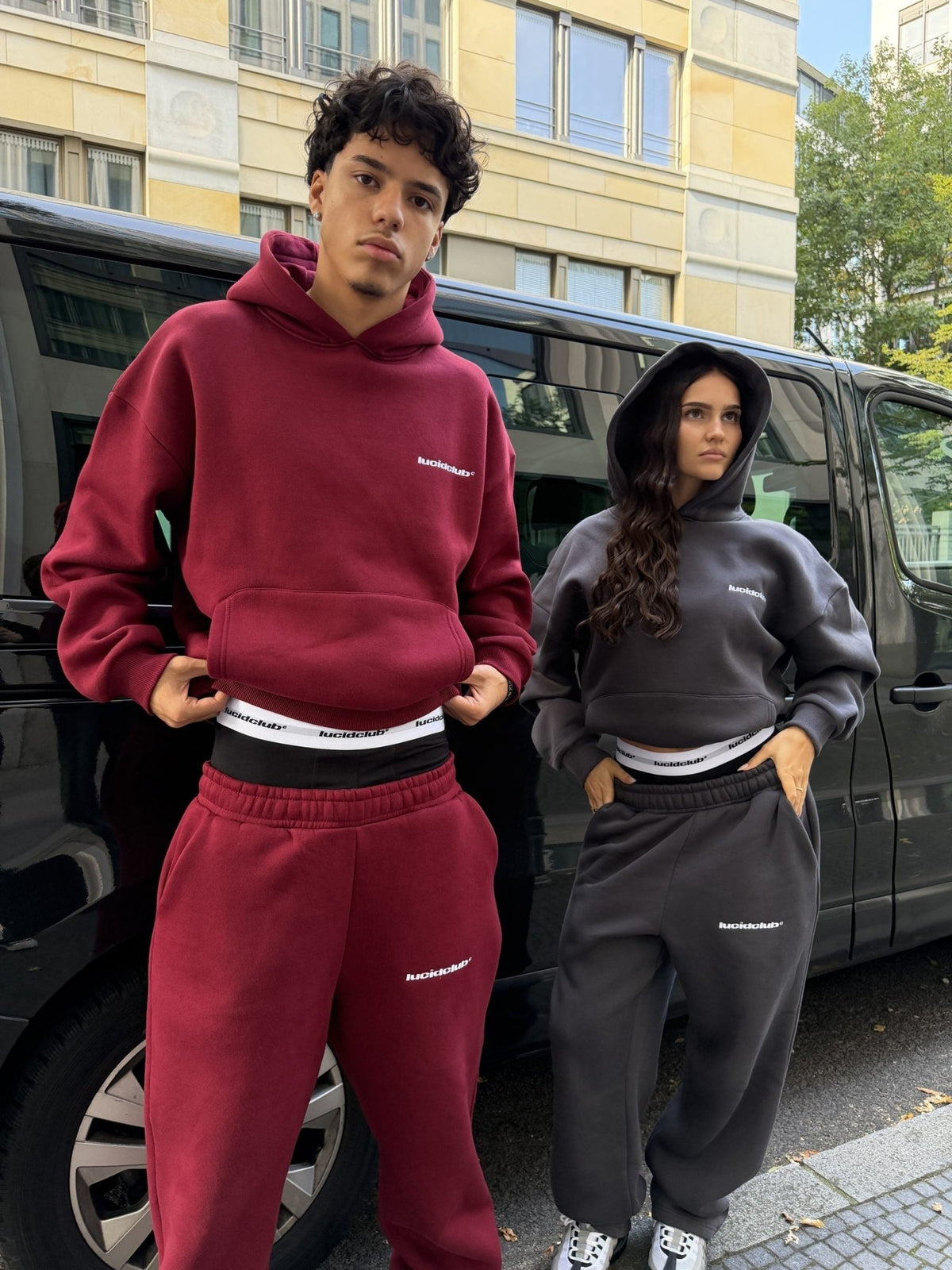 Cozy Tracksuit Wine Red en el modelo, detrás un modelo con Cozy Tracksuit Dark Grey