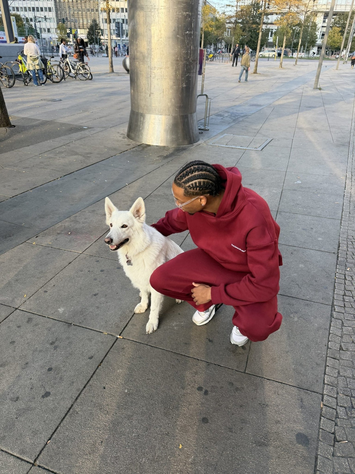 Cozy Tracksuit Wine Red en el modelo, hoodie y pantalón de chándal en granate, junto a un perro blanco en Berlín