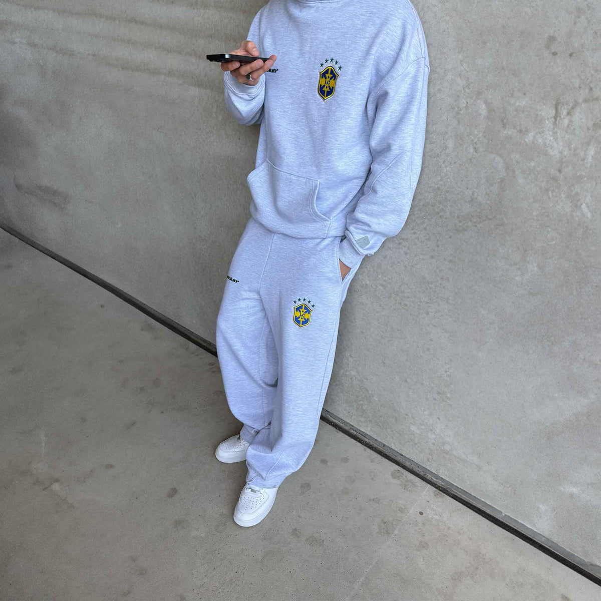 Brazil Hoodie and Brazil Sweatpants Melange Grey on model by a concrete wall