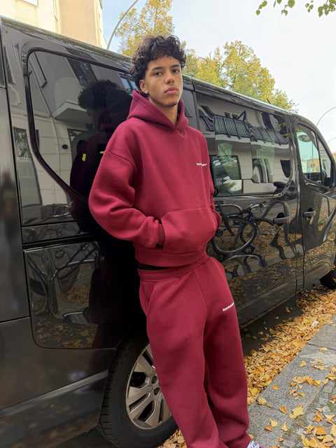 Model im Cozy Tracksuit Wine Red lehnt an einem Van im Herbstlaub