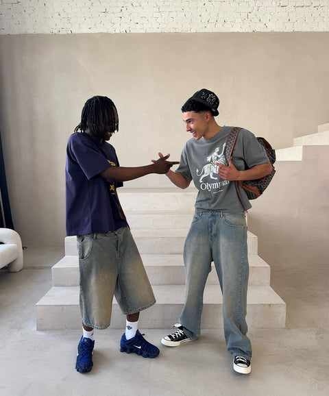Zwei Models im Studio, eins in navy T-Shirt mit Jorts, eins in grauem T-Shirt mit heller Jeans